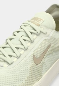 Ανοιχτό πράσινο παπούτσι Nike με υφασμένο επάνω μέρος, επίπεδα κορδόνια και μπεζ λογότυπο Swoosh. Διαθέτει μαξιλαρωμένη γλώσσα και ευέλικτη σόλα.