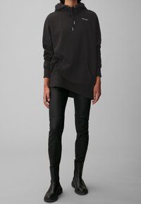 Hoodie noir surdimensionné avec une poche kangourou et un capuchon à cordon réglable, associé à un pantalon en simili cuir noir ajusté et des bottines.