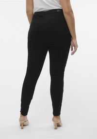 Jeans skinny de tiro alto negros con una textura suave, dos bolsillos traseros y un diseño ajustado, combinados con zapatos de tacón cuadrado beige.