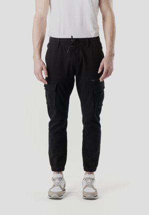 Pantalones cargo negros con cintura elástica, piernas cónicas y múltiples bolsillos laterales. Combinados con zapatillas deportivas blancas y grises.