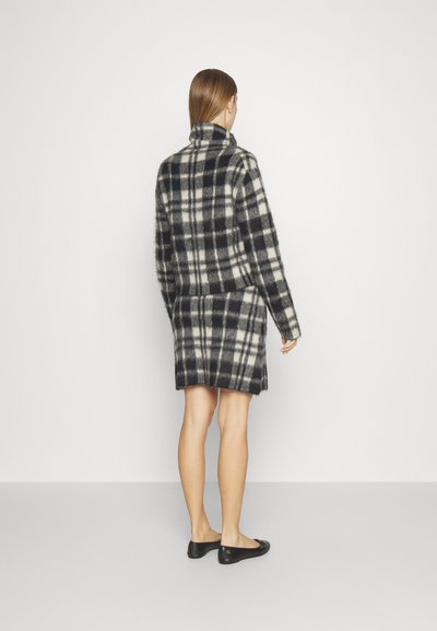 Črno-bele kariraste volnene pulover s visokim ovratnikom, v kombinaciji z ujemajočo se krilom. Obleka se ponaša z mehkobo in ohlapnim fitom.