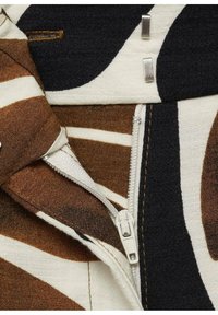 Tissu en toile avec des motifs marron, noir et crème, comportant une fermeture éclair visible et des accents en métal argenté. Surface texturée, design en couches.