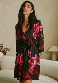 Musta viitta punaisilla kukkakuosisilla yksityiskohdilla, jossa on V-pääntie, pitkät hihat ja sidottava vyötärö. Sujuva kangas, jossa on pehmeä kiilto.