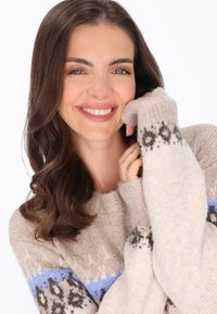 Beige kötött pulóver, kerek nyakkivágással, kék és sötétbarna mintás díszítésekkel az ujjakon és a mandzsettákon. Puha tapintás.