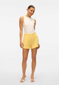Biała bezrękawnikowa bluzka zestawiona z fakturowanymi żółtymi szortami z elastycznym pasem, odpowiednia do codziennego użytku, z lekkiego, przewiewnego materiału.