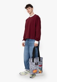 Grå tote-väska med komisk stiltryck, som har svarta remmar och ett tag. Designen inkluderar färgglada accenter och text som visar popkulturteman.