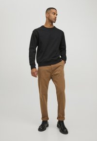 Schwarzer Sweatshirt mit rundem Ausschnitt, kombiniert mit braunen Cordhosen. Schwarze Schnürstiefel. Einfaches Design, einfarbige Farben und lässiger Schnitt.