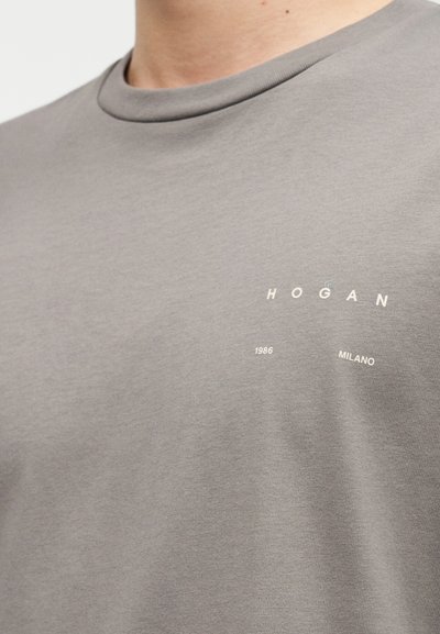 Γκρι βαμβακερό t-shirt με στρογγυλή λαιμόκοψη. Διαθέτει λευκό κείμενο "HOGAN", "1986" και "MILANO" σε μινιμαλιστική διάταξη στο στήθος.
