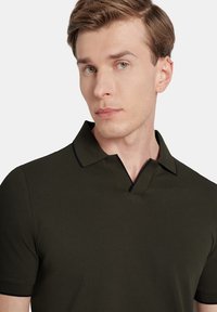 Ciemnozielona koszulka polo z zapięciem na dwa guziki, krótkimi rękawami i kontrastowym czarnym detalem kołnierzyka. Materiał z mieszanki bawełny o teksturowanym wykończeniu.