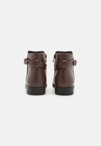 Bottes à cheville en cuir marron avec un bout arrondi, des fermetures éclair latérales et des accents de boucle. Texture lisse et talons empilés noirs.