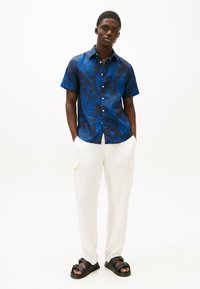 Camicia a maniche corte di colore blu navy con motivo floreale blu, abbinata a pantaloni cargo in lino off-white e sandali neri con fibbie.