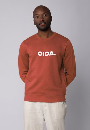 Sweatshirt couleur rouille avec un col rond, arborant le texte blanc "OIDA." sur le devant. Texture douce, poignets et ourlet côtelés.