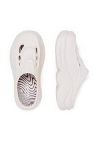 Pantofi albi din material plastic, cu o textură netedă, formă rotundă, detalii decupate pe laturi și o branț cu un model ce conține linii abstracte.