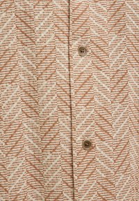 Chemise beige avec un motif texturé de lignes en zigzag marron et de petits points d'accent, dotée de boutons marron clair pour la fermeture.