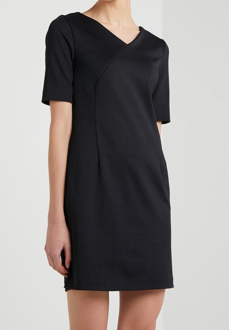 Mustassa mekossa on lyhyet hihat, V-muotoinen pääntie ja viisto sauma-asiat. Valmistettu teksturoituneesta kankaasta, polvenpituinen malli.