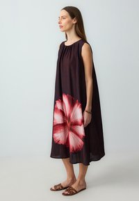 Ein ärmelloses, knielanges Kleid aus dunklem Stoff, das auf der Vorderseite mit einem großen rot-weißen Blumenmuster verziert ist. Einfaches Design und fließende Textur.