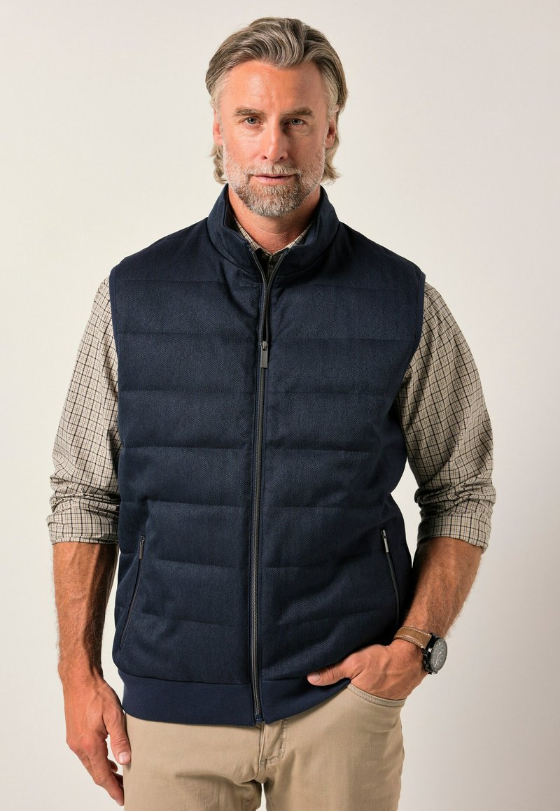 Mörkblå dunstoff med dragkedja fram, sidofickor och ribbad nederkant. Bärs över en rutigt skjorta med ståkrage och vadderat tyg.