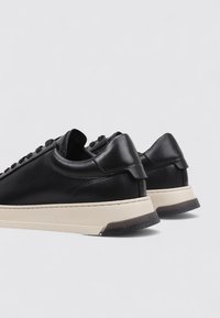 Baskets en cuir noir à profil bas, dotées d'une semelle en caoutchouc crème et d'un design épuré, accentuées par des coutures minimales.