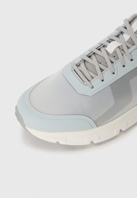 Sapatilha atlética azul clara com um cabedal texturizado, atacadores cinzas e uma biqueira reforçada; projetada com uma sola branca espessa para tração.