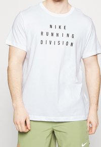 Camiseta de algodón blanca con texto negro que dice "NIKE RUNNING DIVISION". Manga corta y cuello redondo. Diseño simple, sin patrones.