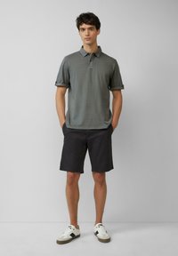 Grau Polohemd mit Kragen und hochgerollten Ärmeln, kombiniert mit dunklen Shorts und weißen Sneakers mit schwarzen Akzenten. Einfaches Design, lässige Passform.