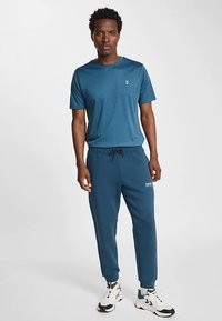 Niebieska sportowa koszulka i dopasowane spodnie dresowe z regulowanym paskiem w talii, ściągaczami przy kostkach oraz małym logo na koszulce.