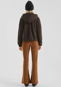 Bruine fleece hoodie met een capuchon en bruine uitlopende broek. Glad oppervlak, aansluitend ontwerp, en een zwarte beanie-hoed maken de outfit compleet.