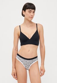 Melna bralette ar V-veida dizainu un regulējamiem siksnām, kas savienota ar ziedu raksta bikini biksītēm ar melnu jostu un baltu apdari.