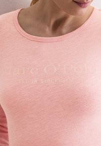 Helles rosa Sweatshirt mit Rundhalsausschnitt und einem weichen, strukturierten Stoff. Auf der Vorderseite befindet sich ein verblasstes Logo in hellem Beige.