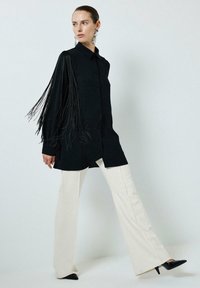 Black button-up shirt with long fringed sleeves, paired with cream flared pants and black pointed heels. Smooth fabric texture and flowy design.