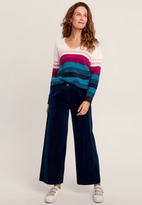 Gestreepte trui in levendig roze, blauw en roomkleur, gecombineerd met donkerblauwe corduroy wijde broek en witte sneakers met drie strapjes.