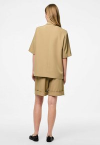 Beige bijpassende set met een korte mouw, colberts zonder kraag en knielange shorts, gemaakt van gladde stof met opgerolde zomen.