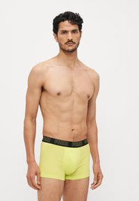 Neon gule boxershorts med en sort elastisk midjebånd som har "PUMA"-logoen. Myk stoff, tettsittende design, middels høyde.
