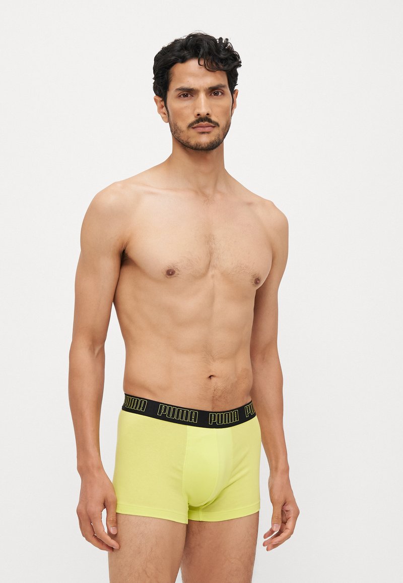 Neon gule boxershorts med en sort elastisk midjebånd som har "PUMA"-logoen. Myk stoff, tettsittende design, middels høyde.
