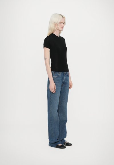 T-shirt nera a maniche corte aderente abbinata a jeans blu con gamba ampia. I jeans hanno un lavaggio chiaro e un design classico a cinque tasche. Scarpe nere completano il look.