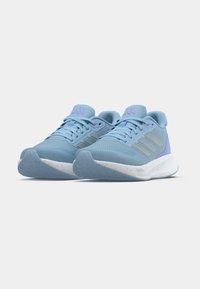 Svijetloplave sportske tenisice s teksturiranim mrežastim gornjim dijelom, trima srebrnim prugama i ljubičastim detaljima. Bijeli potplat s mrljama. Dizajn s niskim izrezom.