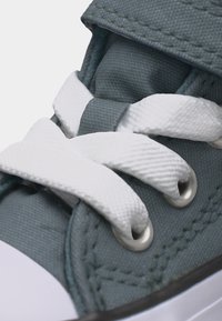 Κοντινή λήψη λευκών κορδονιών παπουτσιών περασμένων μέσα από ασημένιες οπές σε γκρι υφασμάτινο αθλητικό παπούτσι με ορατές λεπτομέρειες ραφών.