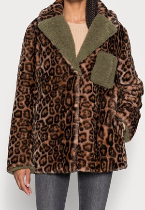 Persona que lleva un abrigo de piel sintética con estampado de leopardo marrón y negro, con cuello y detalles de bolsillo de forro polar verde, combinado con pantalones gris oscuro.