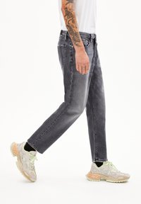 Graue Jeans aus Denim mit lässiger Passform, geraden Beinen und distressed Details, kombiniert mit hellen Sportschuhen mit einzigartigen Aussparungen.