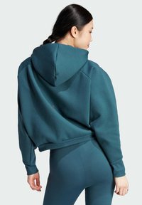Felpa teal con un ampio cappuccio, dalla vestibilità comoda, con polsini e orlo a costine. Abbinata a leggings a vita alta coordinati, entrambi realizzati in tessuto morbido.
