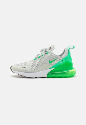 Jasnoszary sportowy sneaker z zielonymi akcentami, siateczkową cholewką, białą podeszwą środkową i przezroczystą zieloną podeszwą z poduszką powietrzną na białym tle.