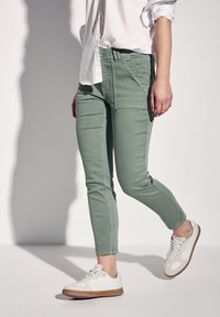 Vaaleanvihreät slim-fit-housut, jotka on valmistettu puuvillasekoitteesta, erottuvat sileällä pinnalla ja taskuilla. Yhdistetty valkoisiin tennareihin ja vaaleaan paitaan.