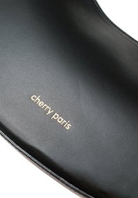 Semelle intérieure en cuir noir avec une texture lisse et une forme arrondie, portant le texte "cherry paris" en doré.