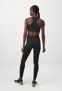 Fekete sportmelltartó, hálós részletekkel, magas derekú fekete leggings-el párosítva, texturált panelek és testhez simuló kialakítás jellemzi. A fekete tornacipők hozzák véglegessé a megjelenést.