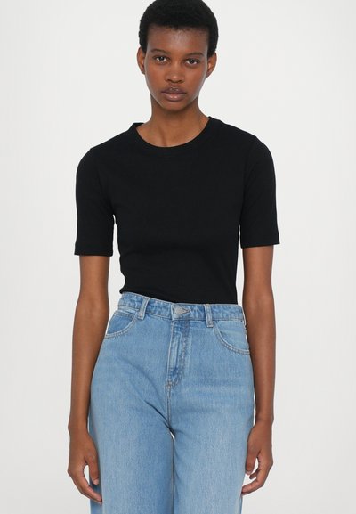 Schwarzes T-Shirt mit kurzen Ärmeln und rundem Ausschnitt, kombiniert mit hellblauen, hochgeschnittenen Jeans; legere, figurbetonte Silhouette mit subtiler Textur.