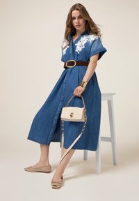 Denim jurk met korte mouwen, witte bloemenborduursels, een bruin ceintuur, gecombineerd met beige flats en een lichte handtas.