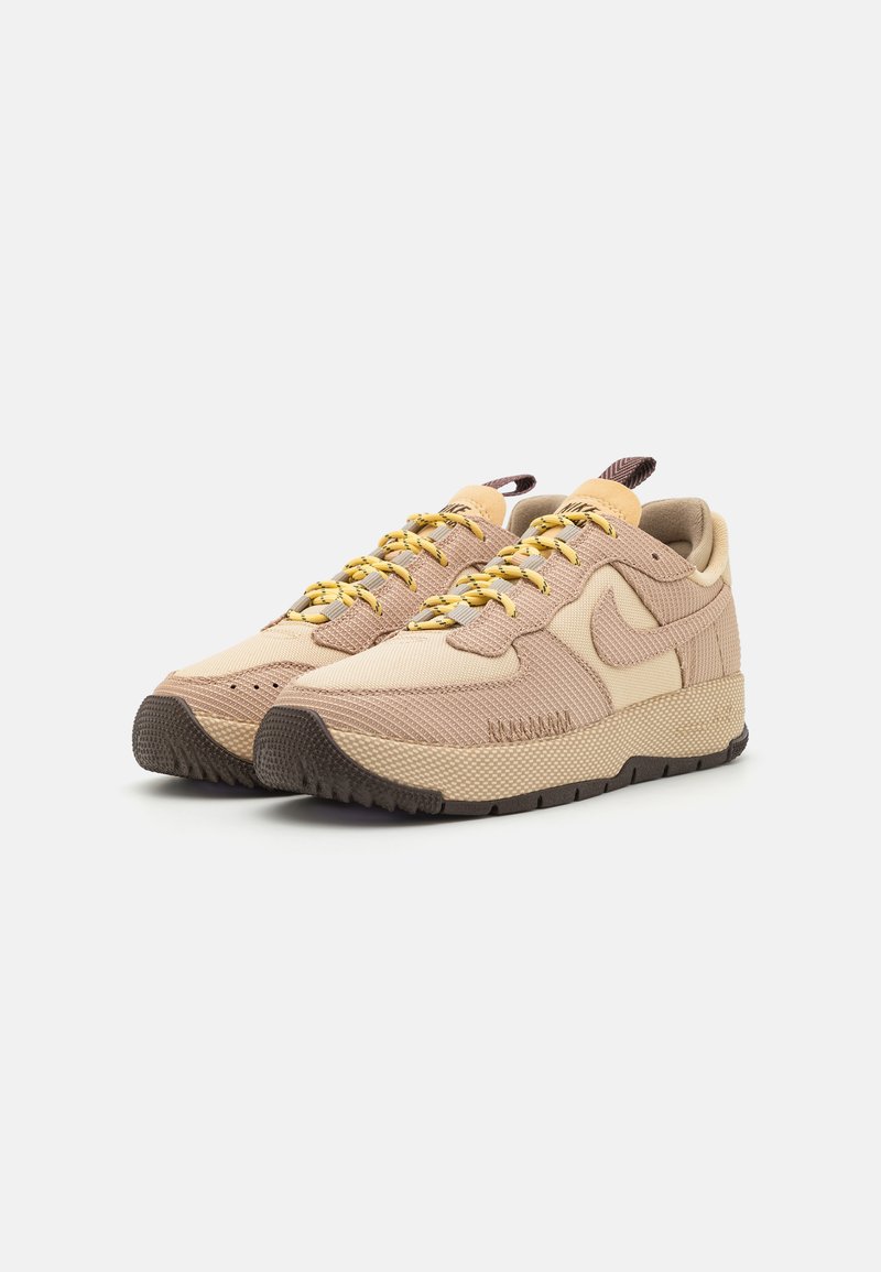 Sneakers Nike beige con tessuto testurizzato, lacci gialli e suola in gomma. Presentano un design curvo distintivo e un logo cucito.