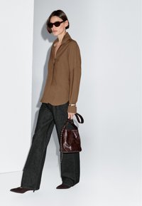Brown long-sleeve shirt with a collar, dark wide-leg pants, and a brown leather bag with a patterned strap. Accessories include dark sunglasses.