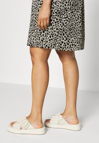 Sandales à glissière beige clair avec une texture froncée sur le dessus, dotées d'une semelle épaisse et rembourrée ainsi que d'un design minimaliste.