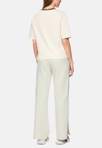 Pale pink short-sleeve top with leopard-patterned neckline, paired with cream wide-leg pants featuring side slits, worn with white shoes.